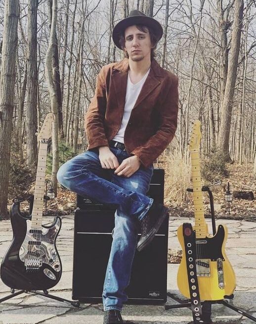 Guy sitting on an amp with a Telecaster and and Strat